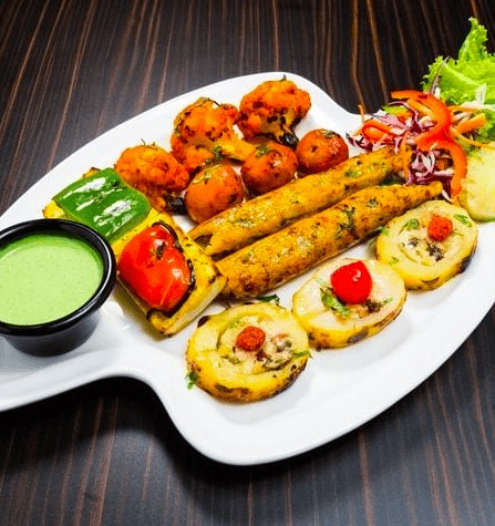An assortment of Paneer Tikka, Onion Pakora, Samosa, Spring Rolls, and Papad